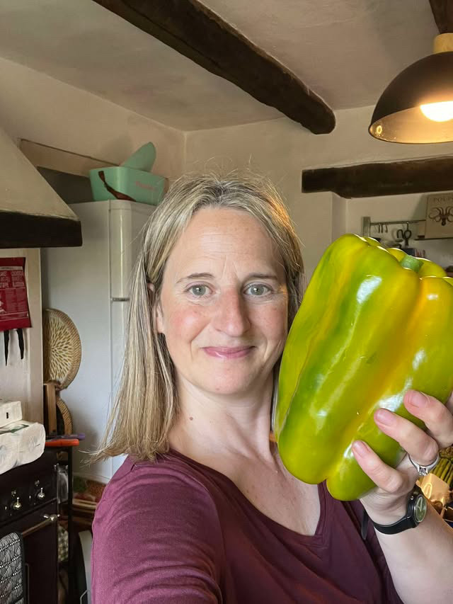 Kirsten, the retreat chef, smiling in a farmhouse kitchen and holding up a large green pepper