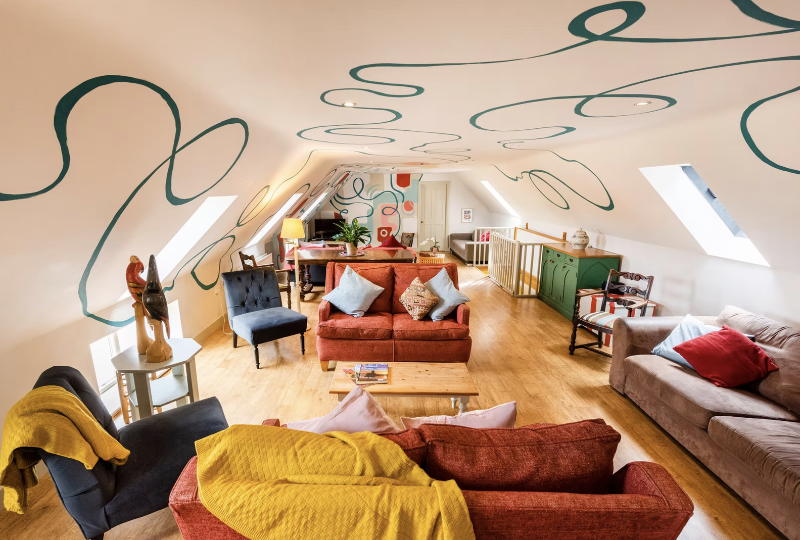 Bright attic living room with red sofas and playful teal line murals on the ceiling