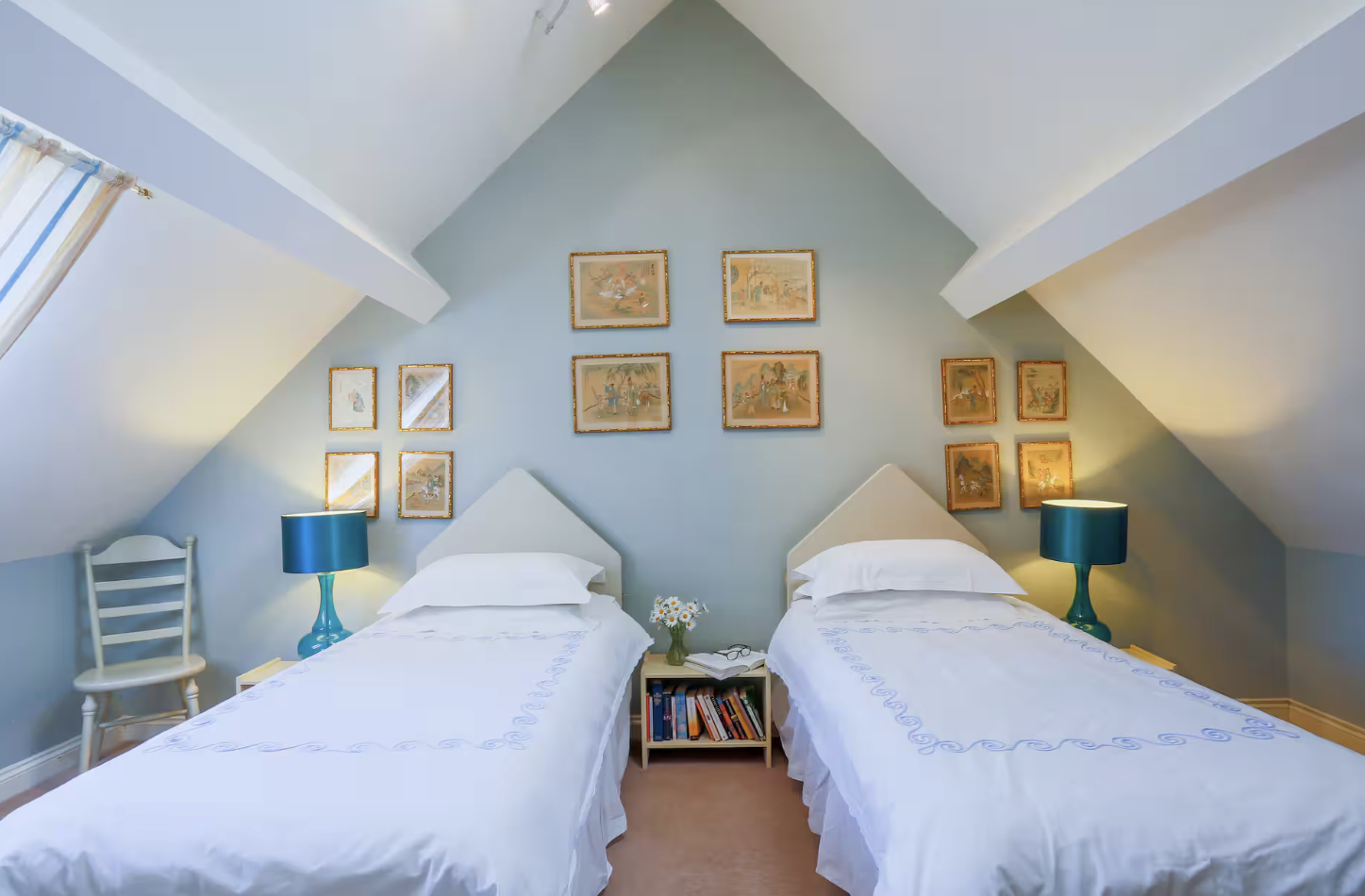 Twin bedroom with two single beds, pale blue walls and gold-framed pictures