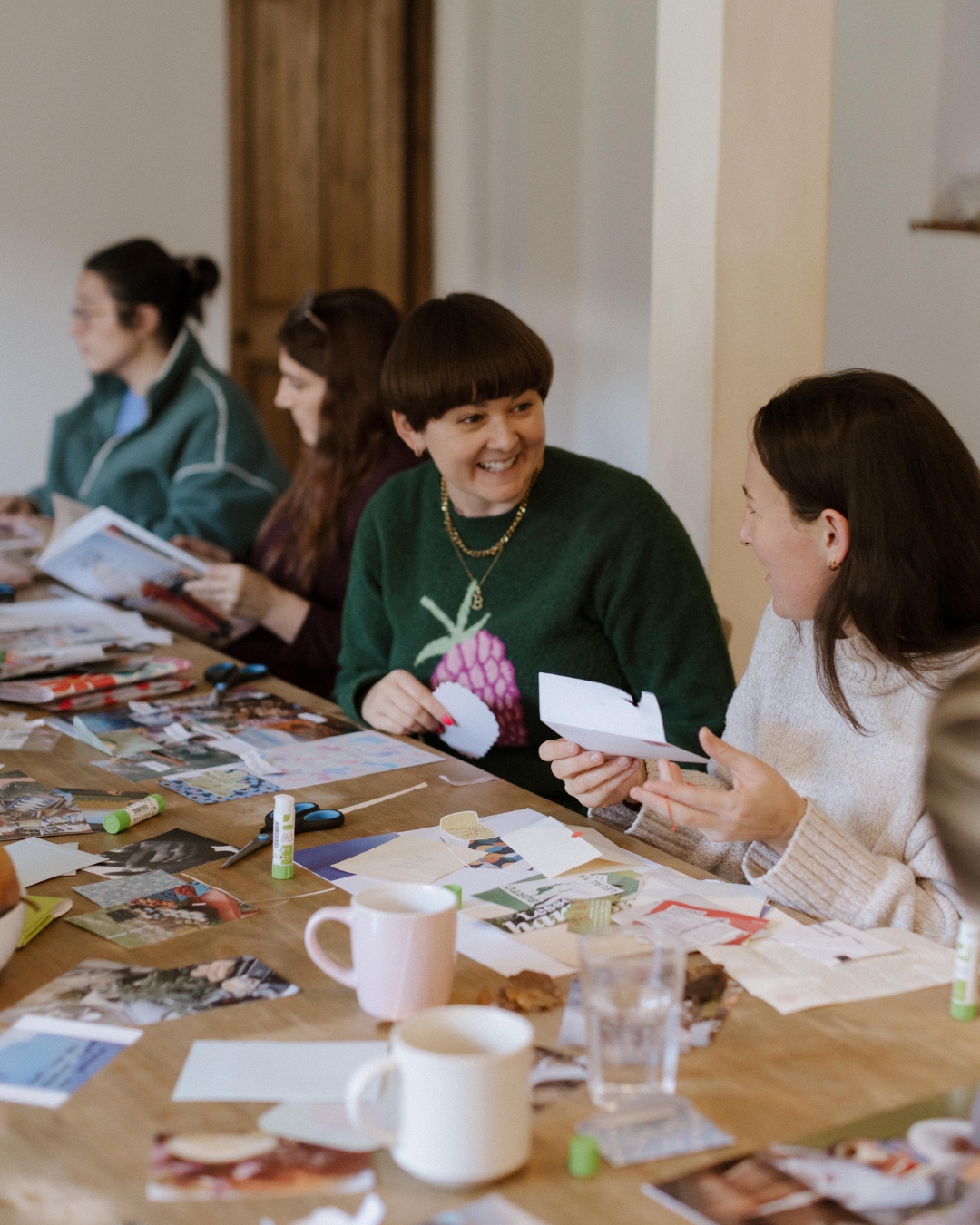 Beth laughing with participants around a table covered in collage materials