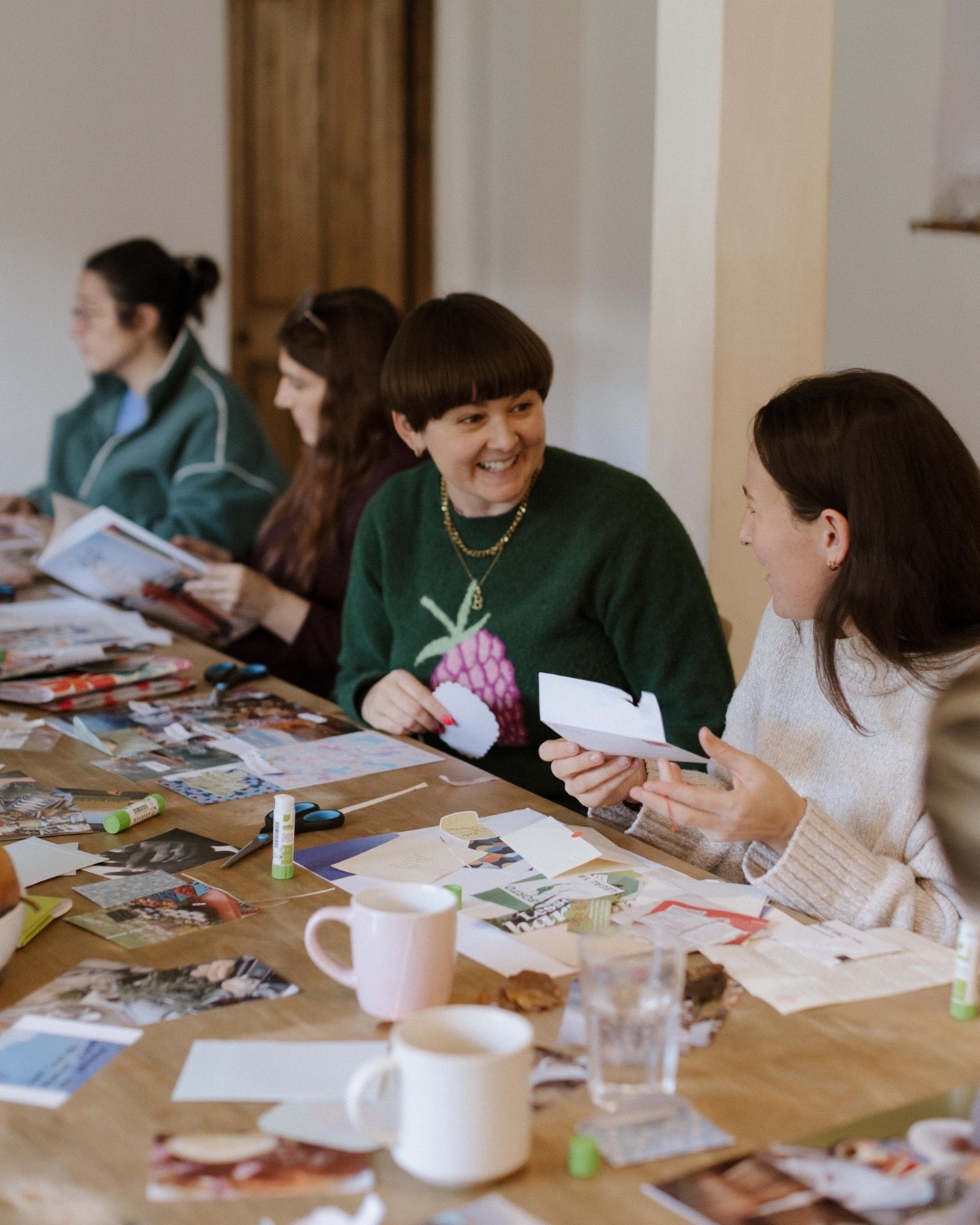 Beth laughing with participants around a table covered in collage materials